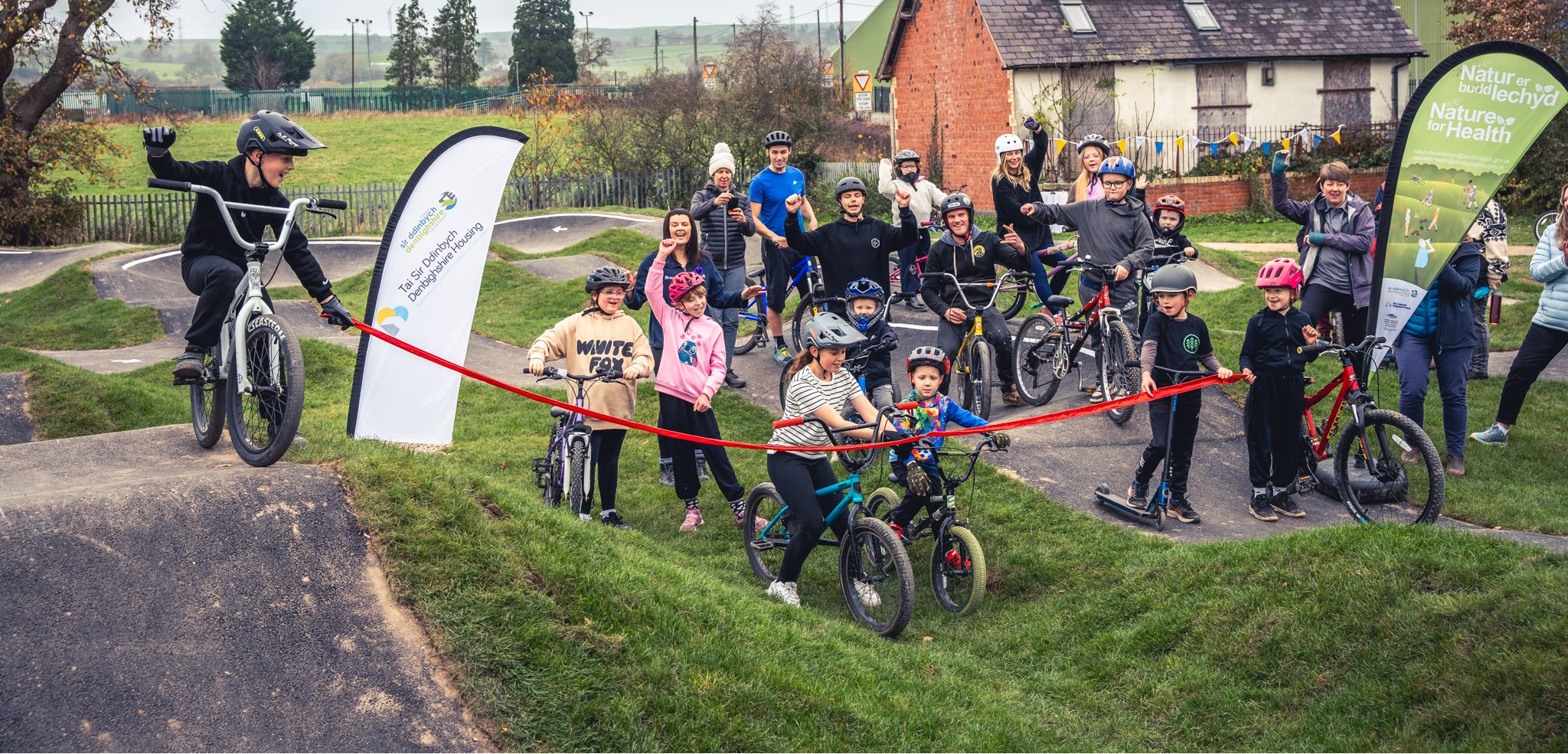 A group of children and adults celebrate behind a red rope for the Actif Denbighshire Project.