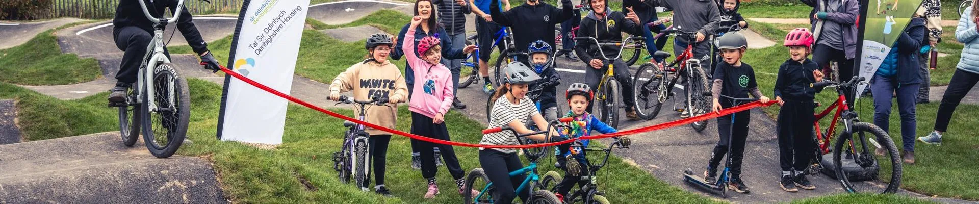 A group of children and adults celebrate behind a red rope for the Actif Denbighshire Project.