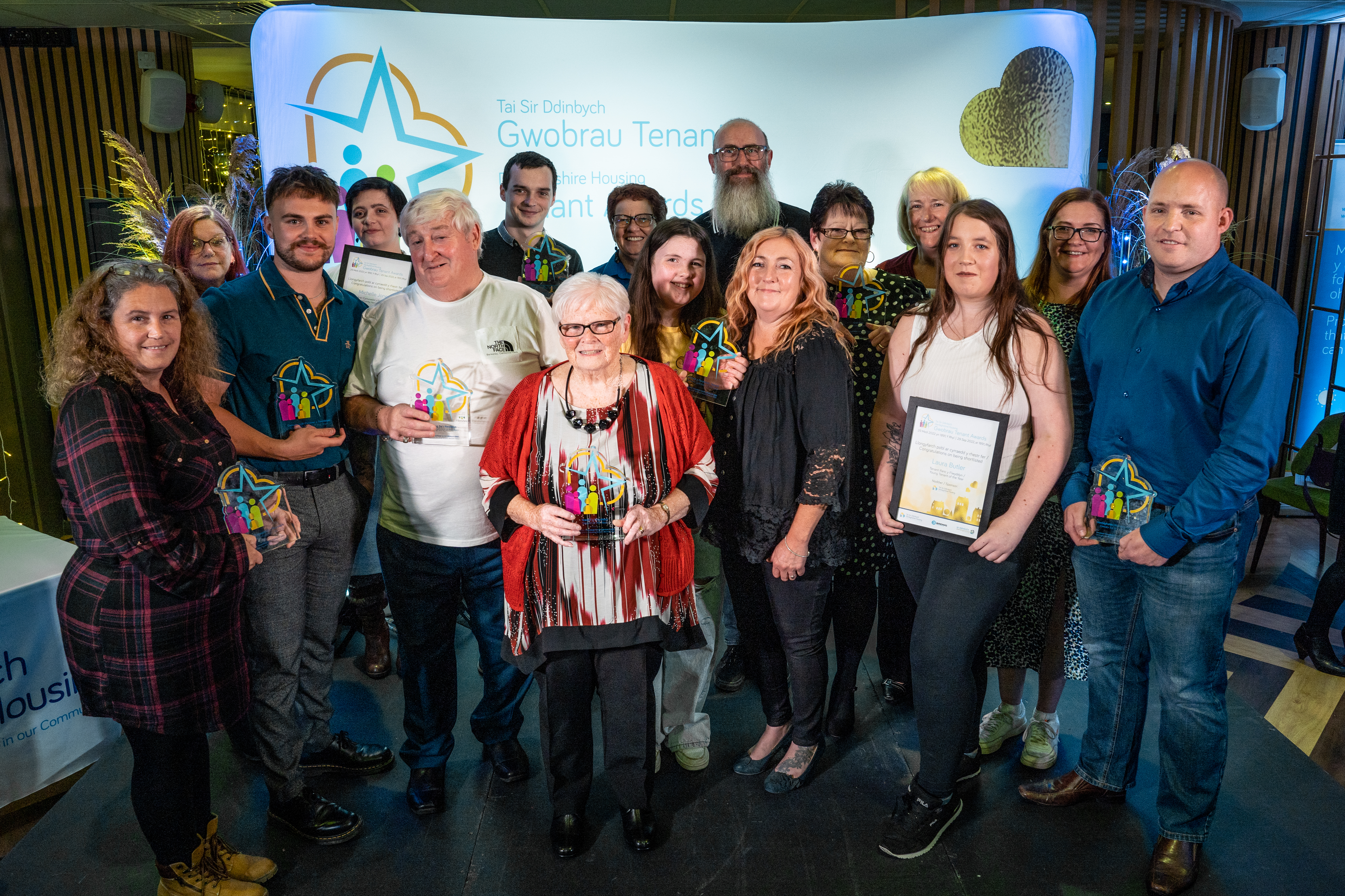 A group of people smiling and holding glass awards at the Denbighshire Housing and Tenancy awards event.