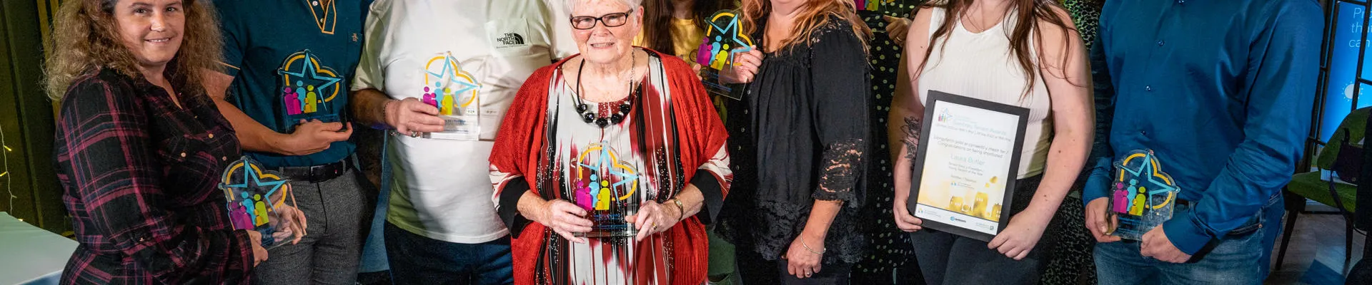 A group of people smiling and holding glass awards at the Denbighshire Housing and Tenancy awards event.