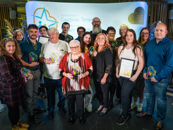 A group of people smiling and holding glass awards at the Denbighshire Housing and Tenancy awards event.
