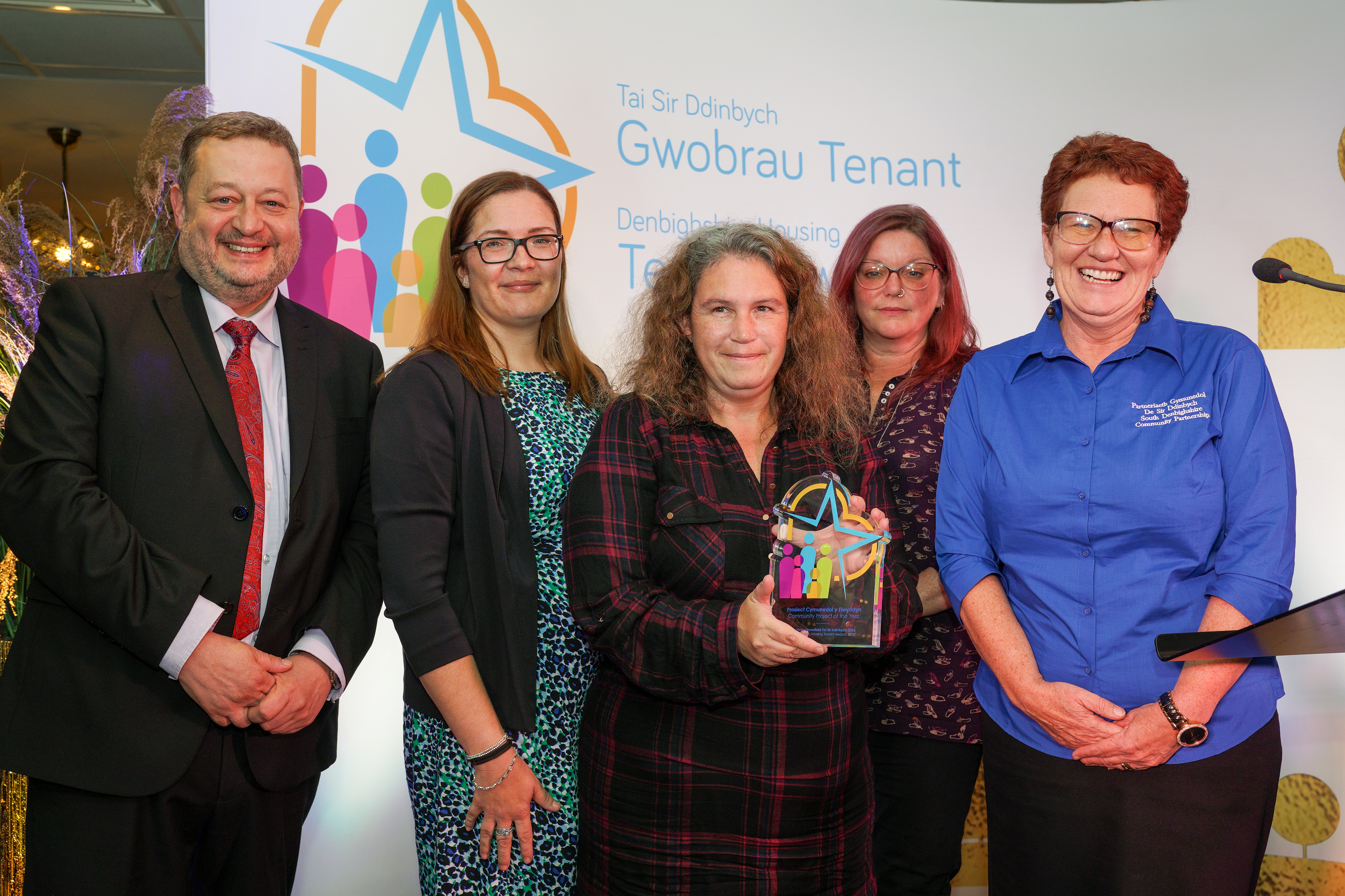 Five people stood together, with a woman in the centre holding a colourful glass award at the 2022 tenant awards event.