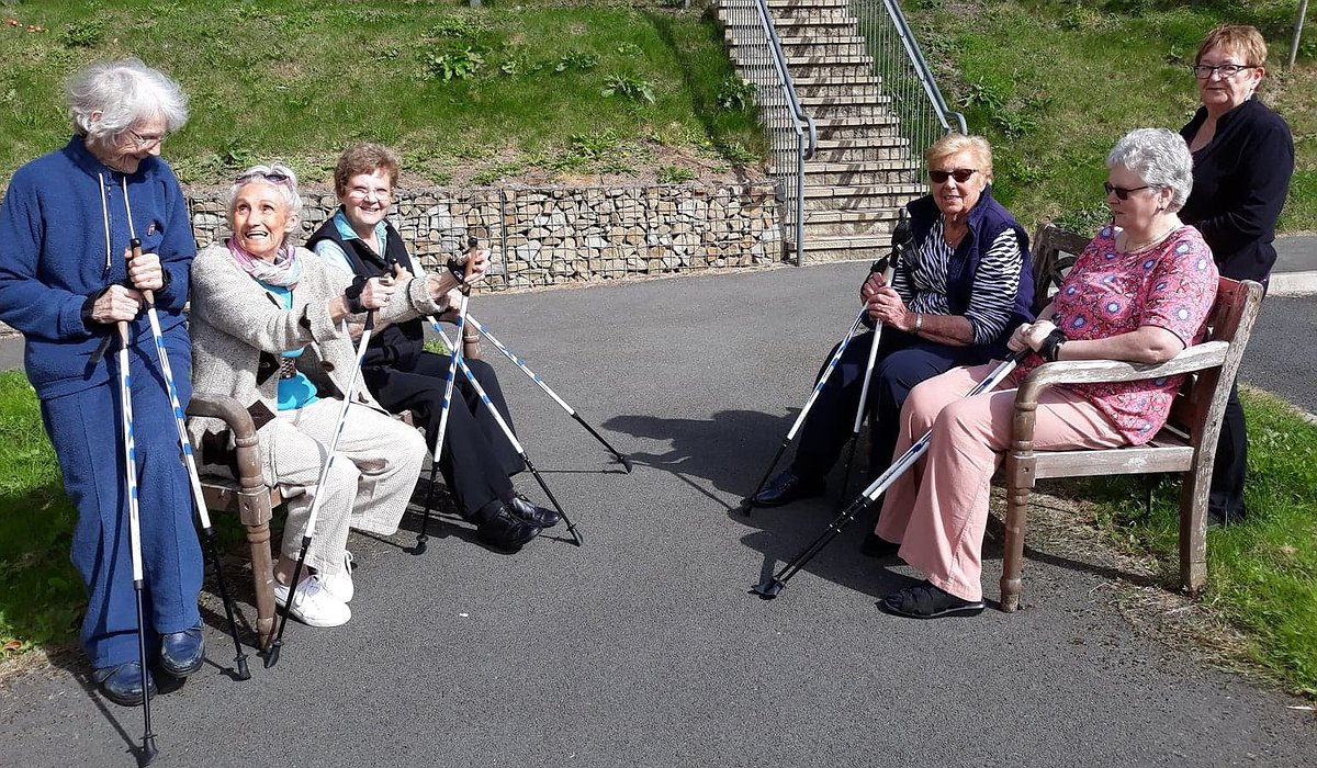 A small group of older women outside, holding walking sticks and taking part in armchair exercises