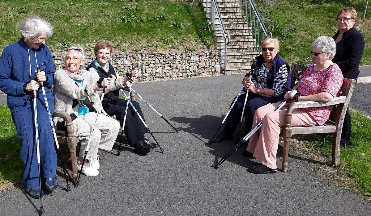 A small group of older women outside, holding walking sticks and taking part in armchair exercises