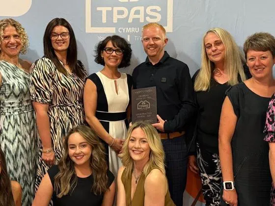 A group of people stand together with the TPAS Cymru Good Practice Award plaque.