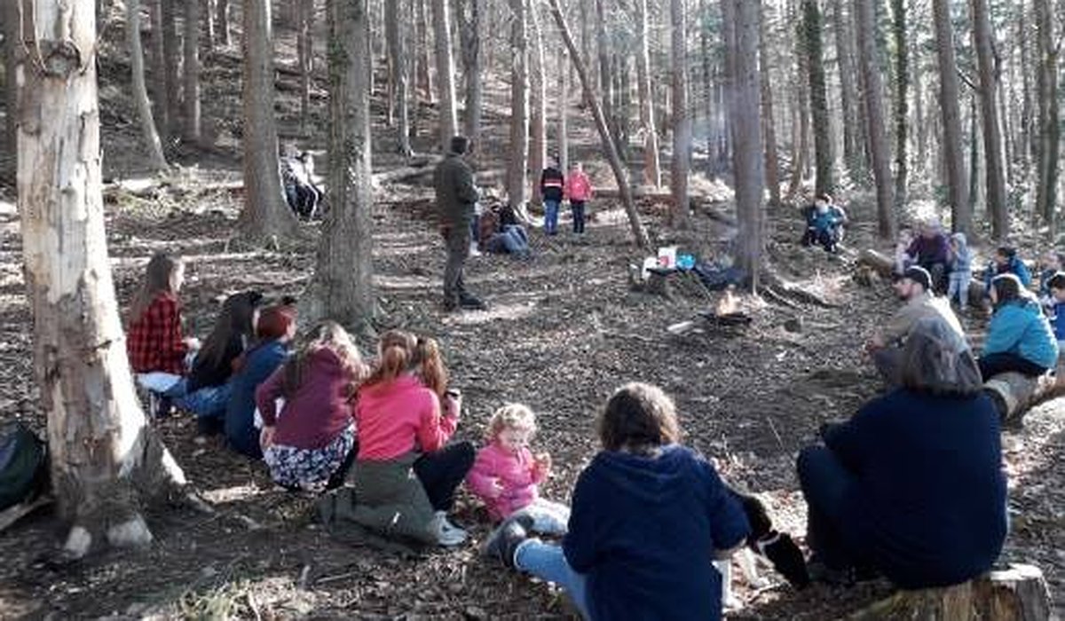 A group of children and adults having breakfast in the woods.