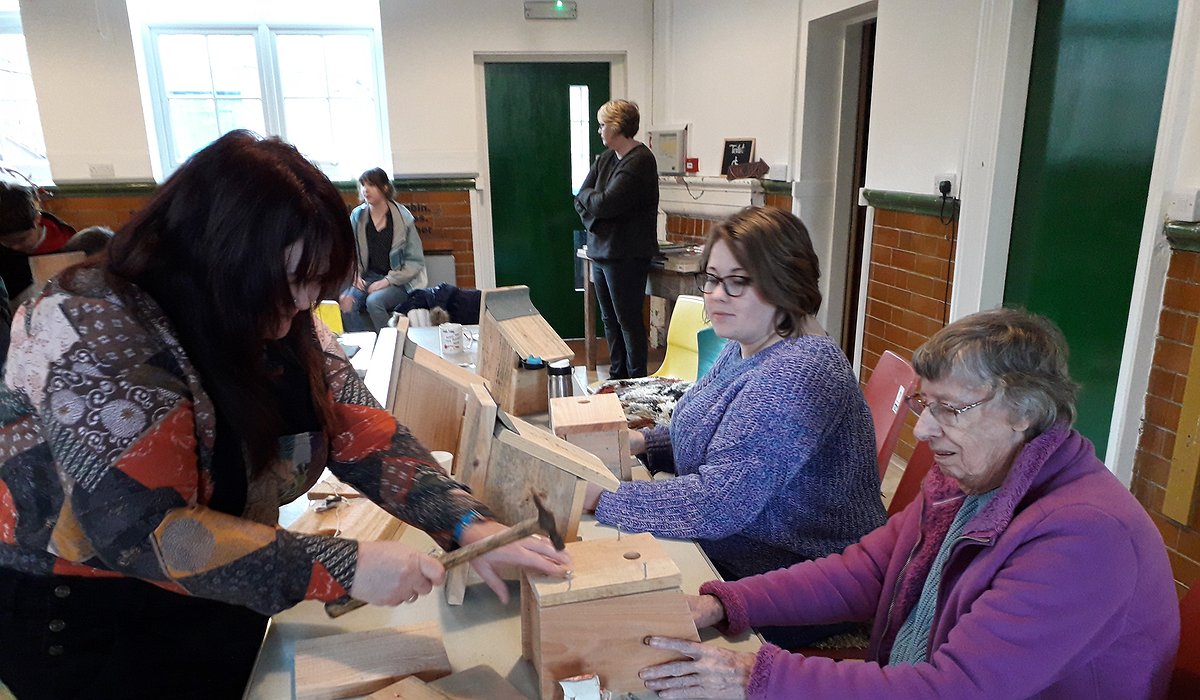 A small group of women sitting at tables in a community centre building bird boxes as part of the Nature for Health project.