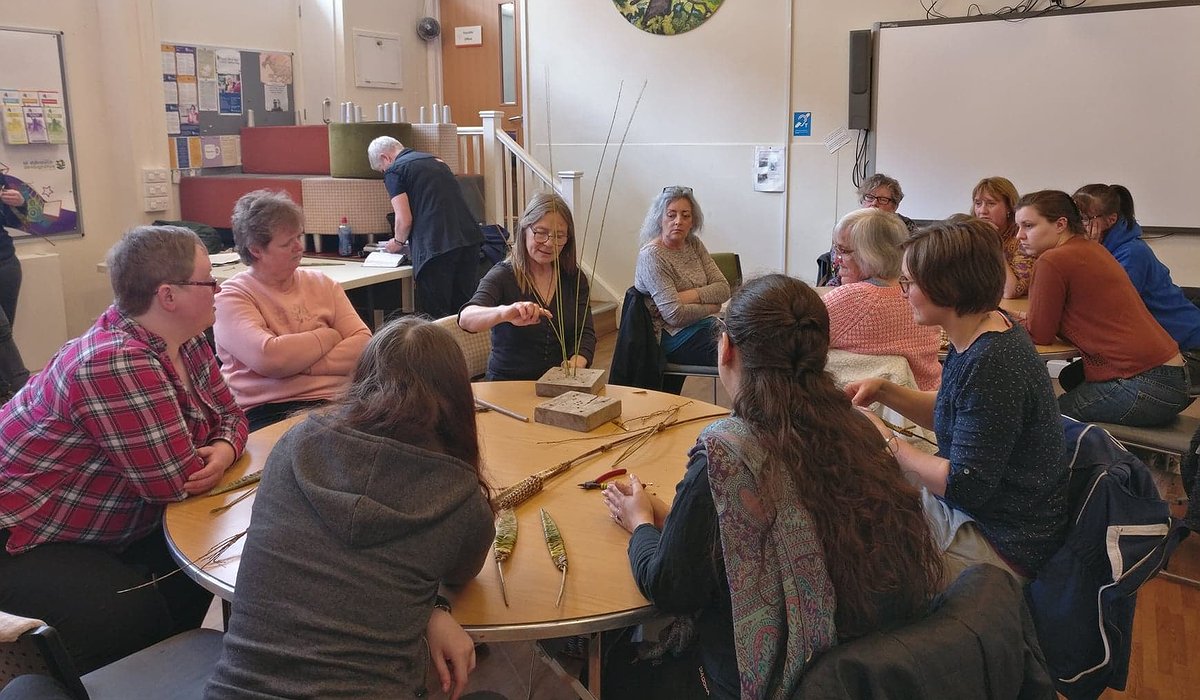 A small group of adults sitting at tables in a Community Centre in Corwen learning to willow weave, part of the Nature for Health project.