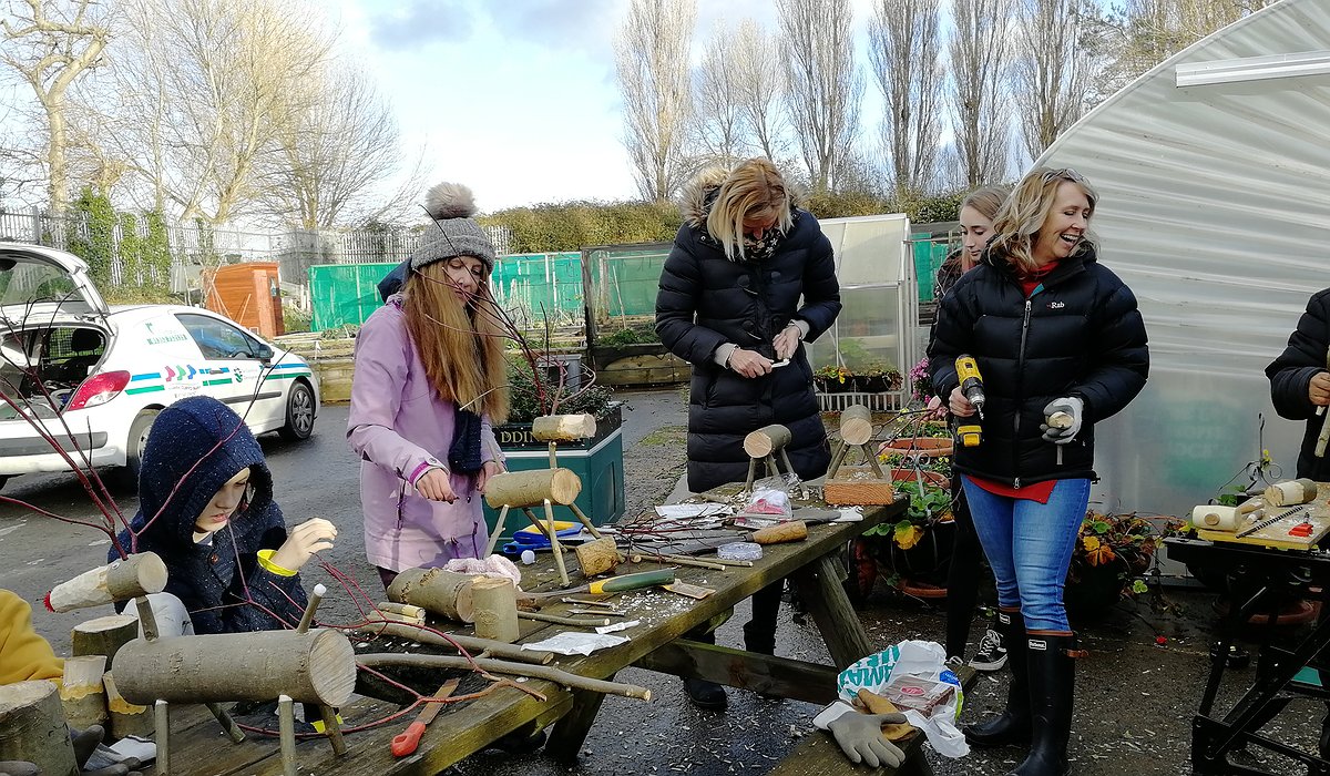 Three children and an adult making wooden reindeer from logs at Morfa Gateway and part of the Nature for Health project.