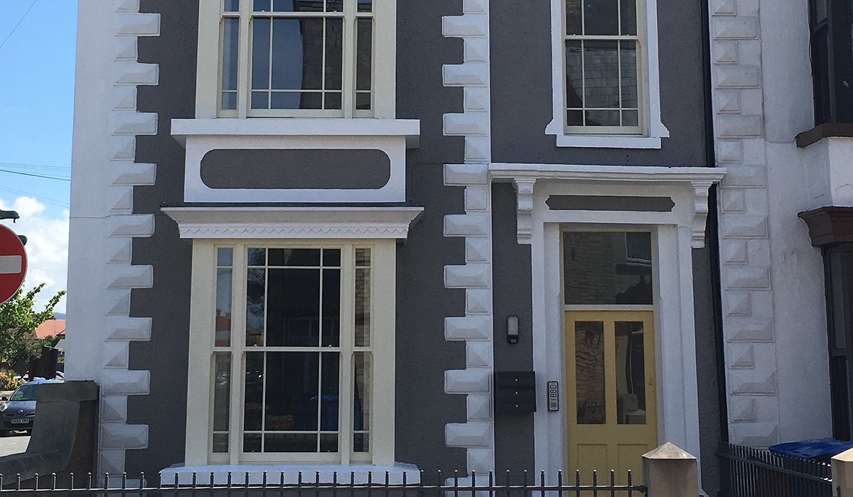 Semi-detached, 3 storey flats, with grey exterior and white brickwork around the edges of the windows.