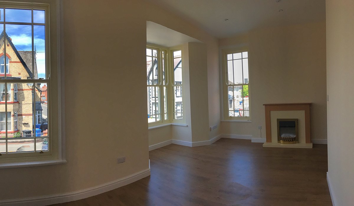 Cream coloured room with fireplace and 3 windows.